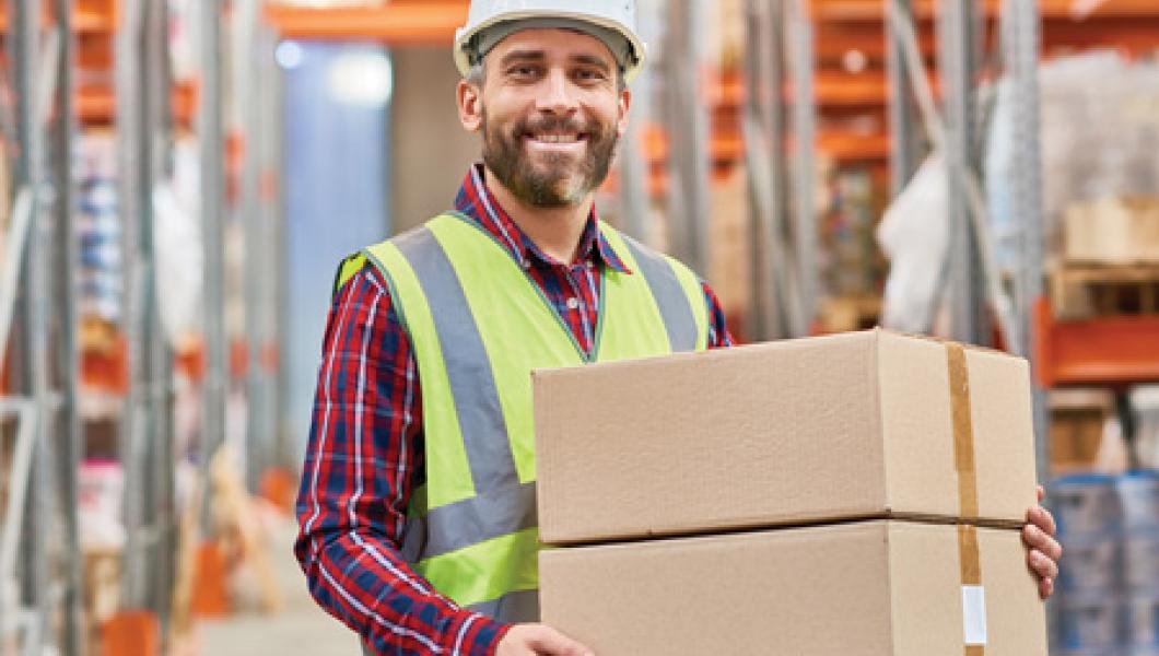 Man smiling, wearing safety gear, and carrying boxes
