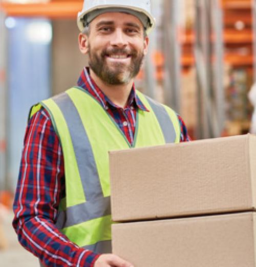 Man smiling, wearing safety gear, and carrying boxes